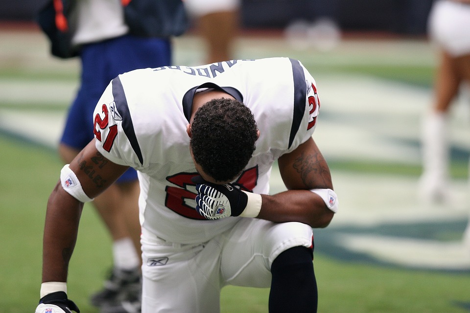 American Football player on one knee with head in hand