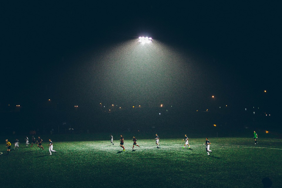 Football pitch at night, players running in the rain, flood light on